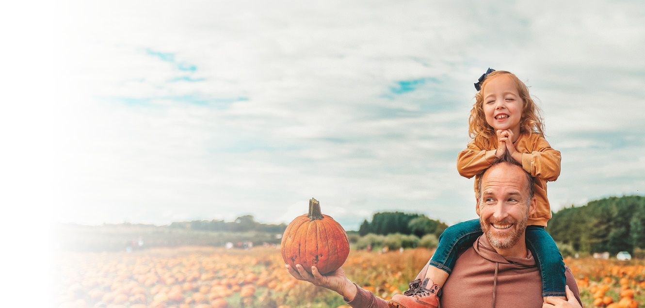 image of a pumpkin patch with a dad holding a pumpkin and his daughter on his shoulders
